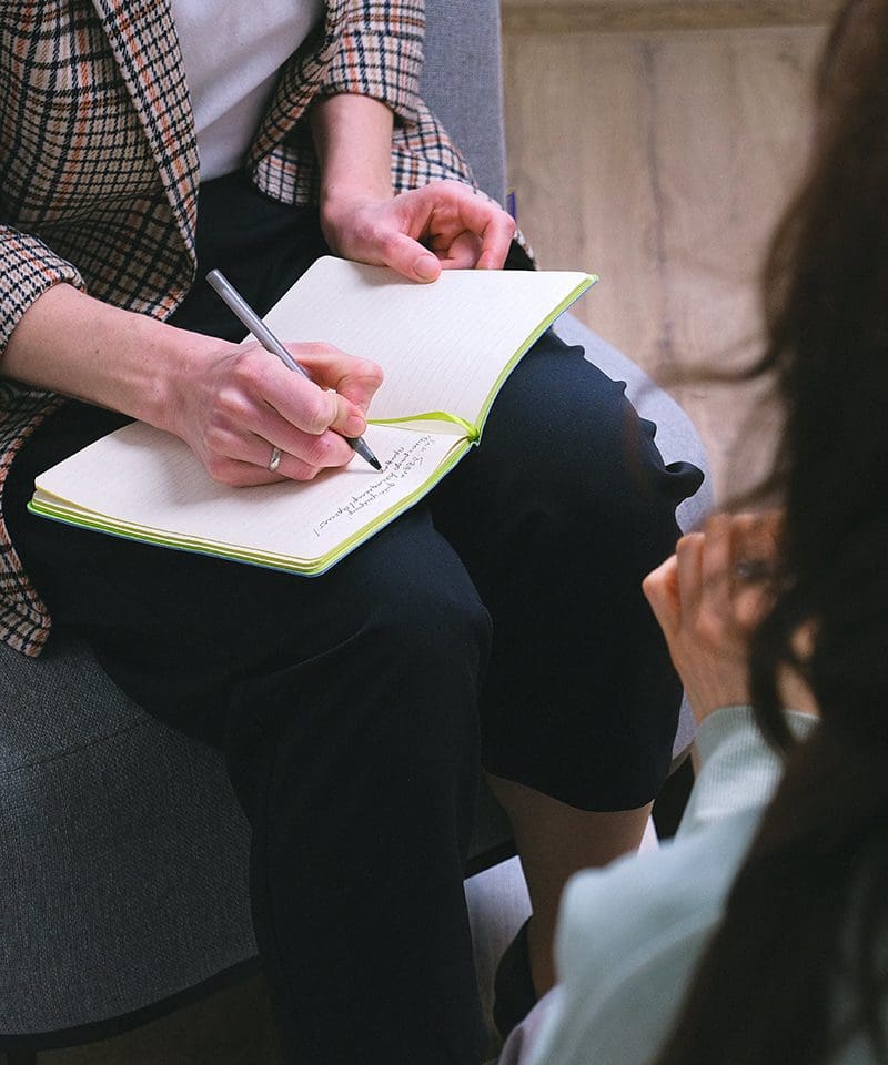 A person writing in a notebook while sitting on the ground.